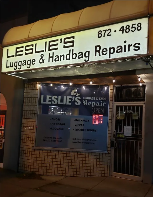 The shop front at night, with the lit sign: Leslie's Luggage & Handbag Repairs, 872-4858